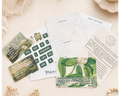 A styled flat-lay of a Bible study or prayer card set on a warm cream fabric background, surrounded by dried flowers, a lit candle, and wooden beads. The set includes printed cards with scripture verses, a writing guide, and a green botanical-themed card.